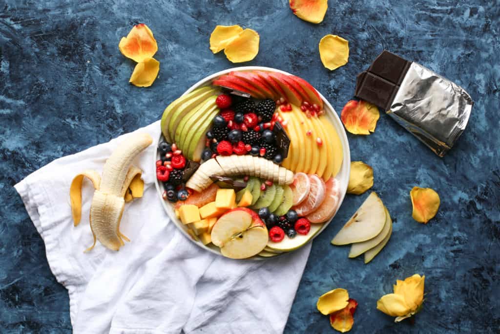 Picture of fresh fruit arranged on a plate surrounded by chocolate bar and more fruit