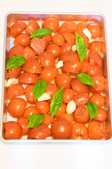 Picture of tomatoes, garlic and basil laves arranged in a single layer on a sheet pan