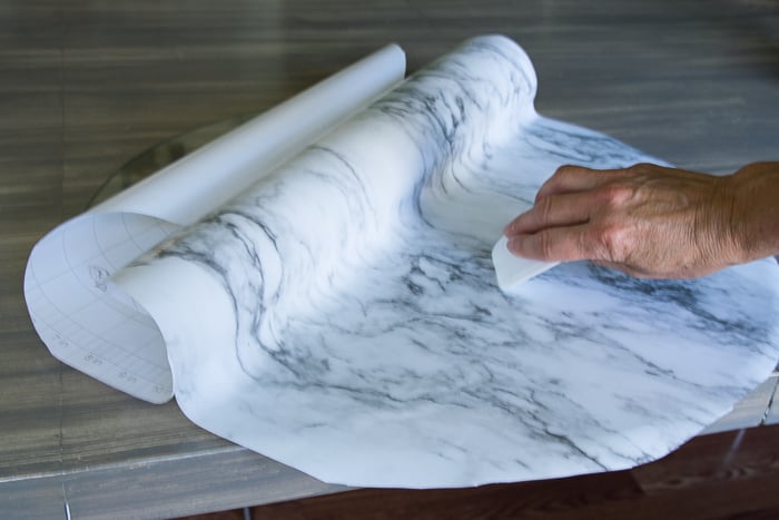 picture showing marble shelf liner paper applied to table round with plastic dough scraper