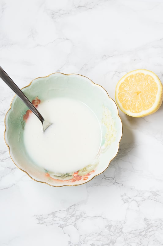 lemon icing in a bowl and a half fresh lemon