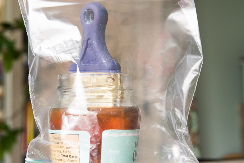 brush soaking in a glass jar of brush cleaner covered by zip bag