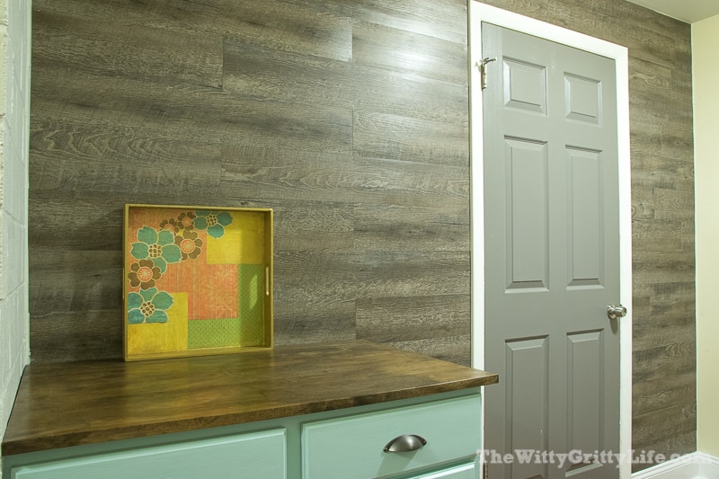 Adding an easy and budget friendly planked wall is easier than you think! Planked walls are not only trendy, but practical as well. This DIY planked wall is the perfect solution for a laundry room and can cover up uneven unsightly walls. No special tools or skills required. Inexpensive vinyl floor tiles make this wall easy to install and care for!