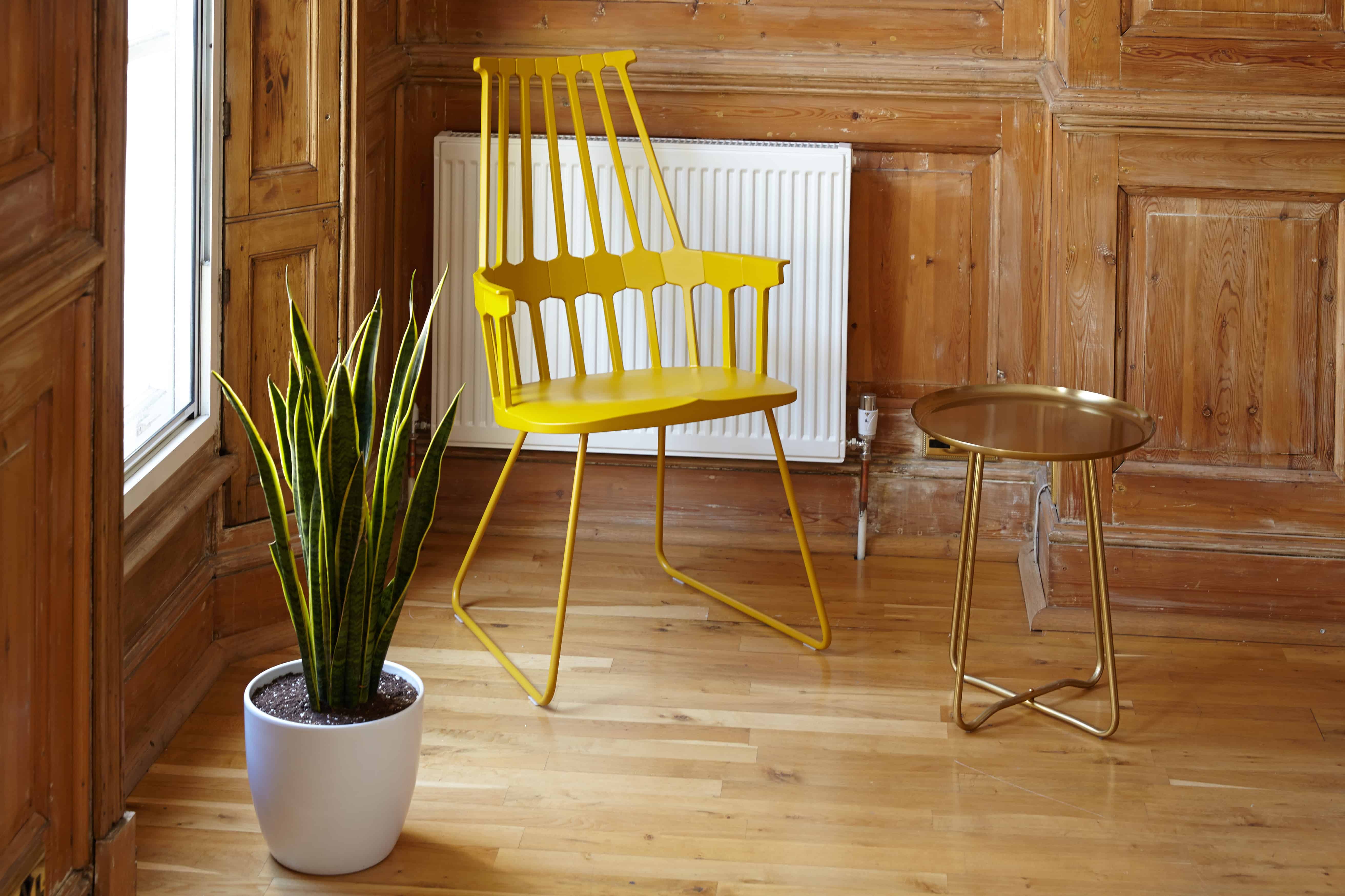 corner of a wood paneled room featuring a whimsical yellow chair, metal side table and white planter with a snake plant