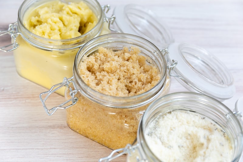 three open jars containing bath salts, body balm, and sugar scrub