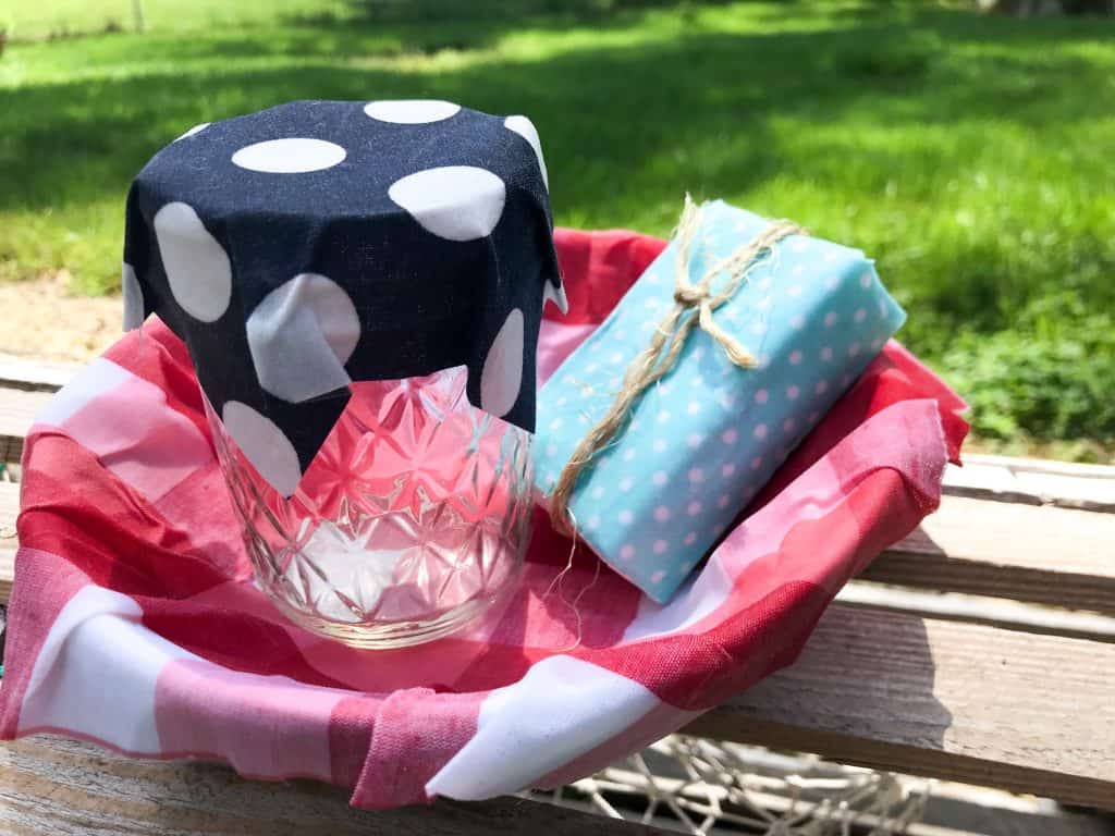 picture showing a bowl lined with red and white checker fabric holding a jar with blue and white polka dot cover and a bar of soap wrapped in light blue fabric and twine