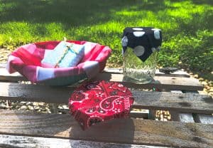 picture showing wax fabric lined bowl, small bowl covered in waxed bandana fabric, bar of soap wrapped in wax fabric and jelly jar with blue and white ploka dot cover