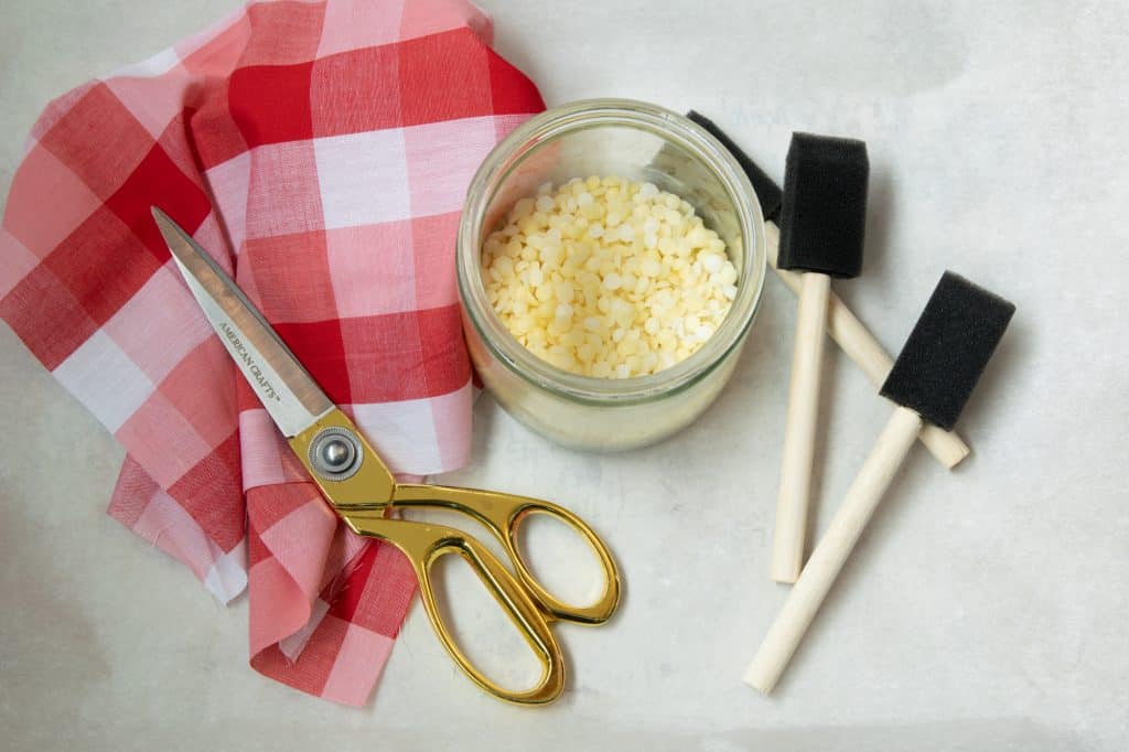 red and white cloth, scissors, bees wax pellets in a glass jar and three foam craft brushes