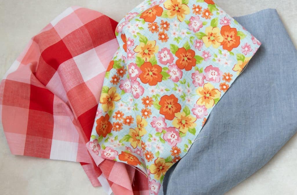 Three different fabrics from left to right: red and white checker, orange and light blue flower, chambray