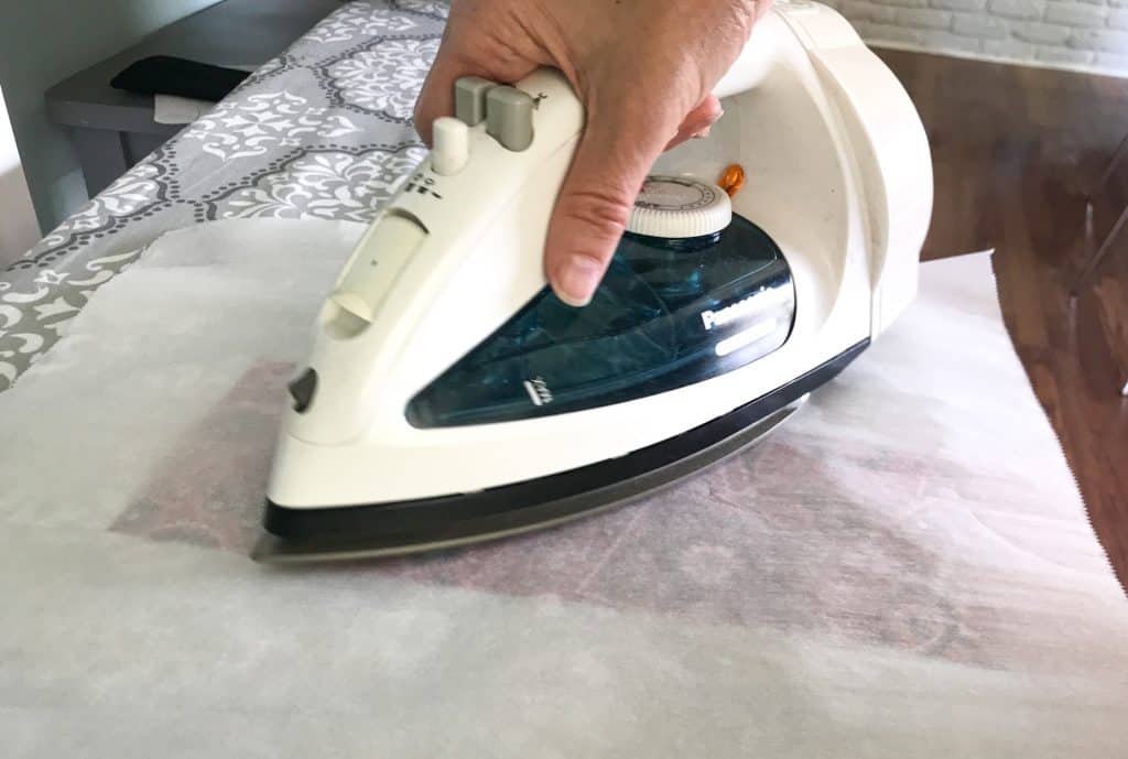 picture of hand holding iron and ironing cloth with wax sandwiched between two layers of parchment paper