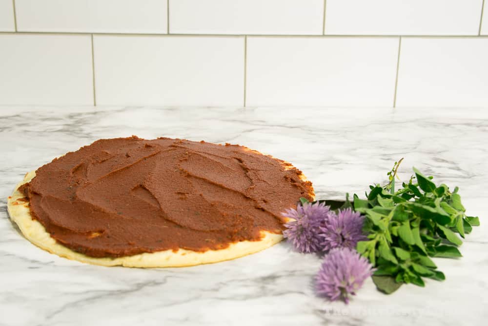 pizza crust with sauce on top and fresh herbs next to it