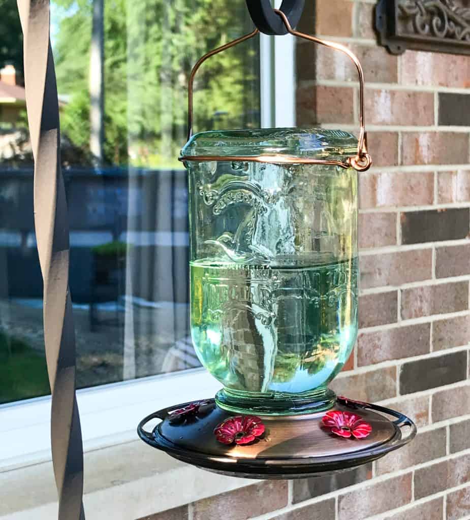 Picture of a mason jar hummingbird feeder hanging in front of a window.