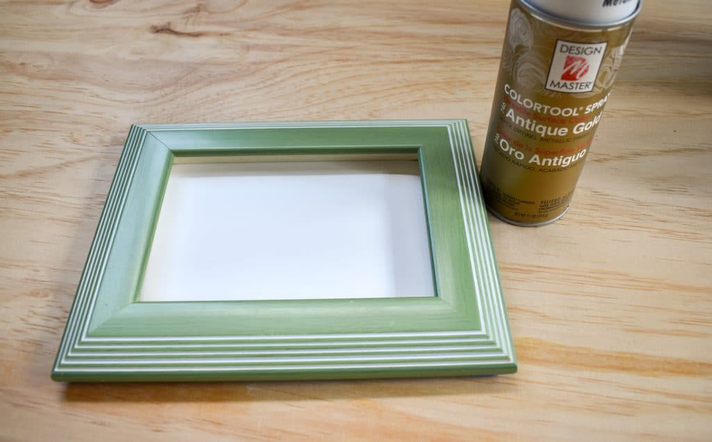 image showing light green picture frame and gold spray paint can on a wood background