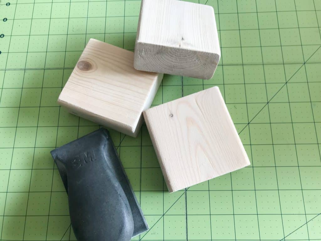 image of three small square wood blocks and sanding tool on a lined cutting mat